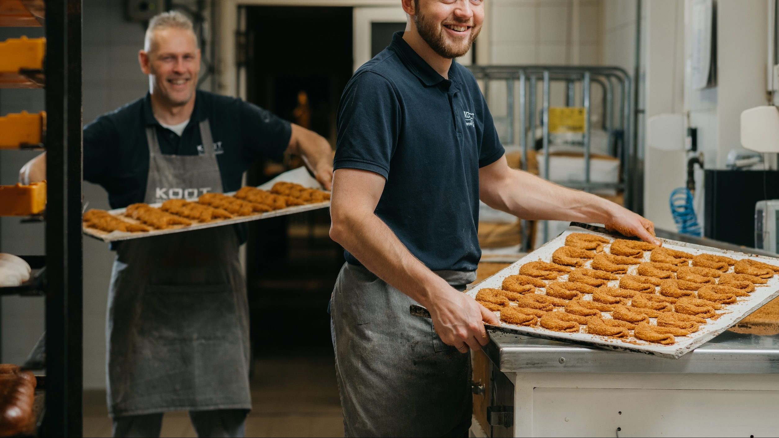 Twee bakkers van Bakkerij Koot met bakplaten vol versgebakken Haantje Pik